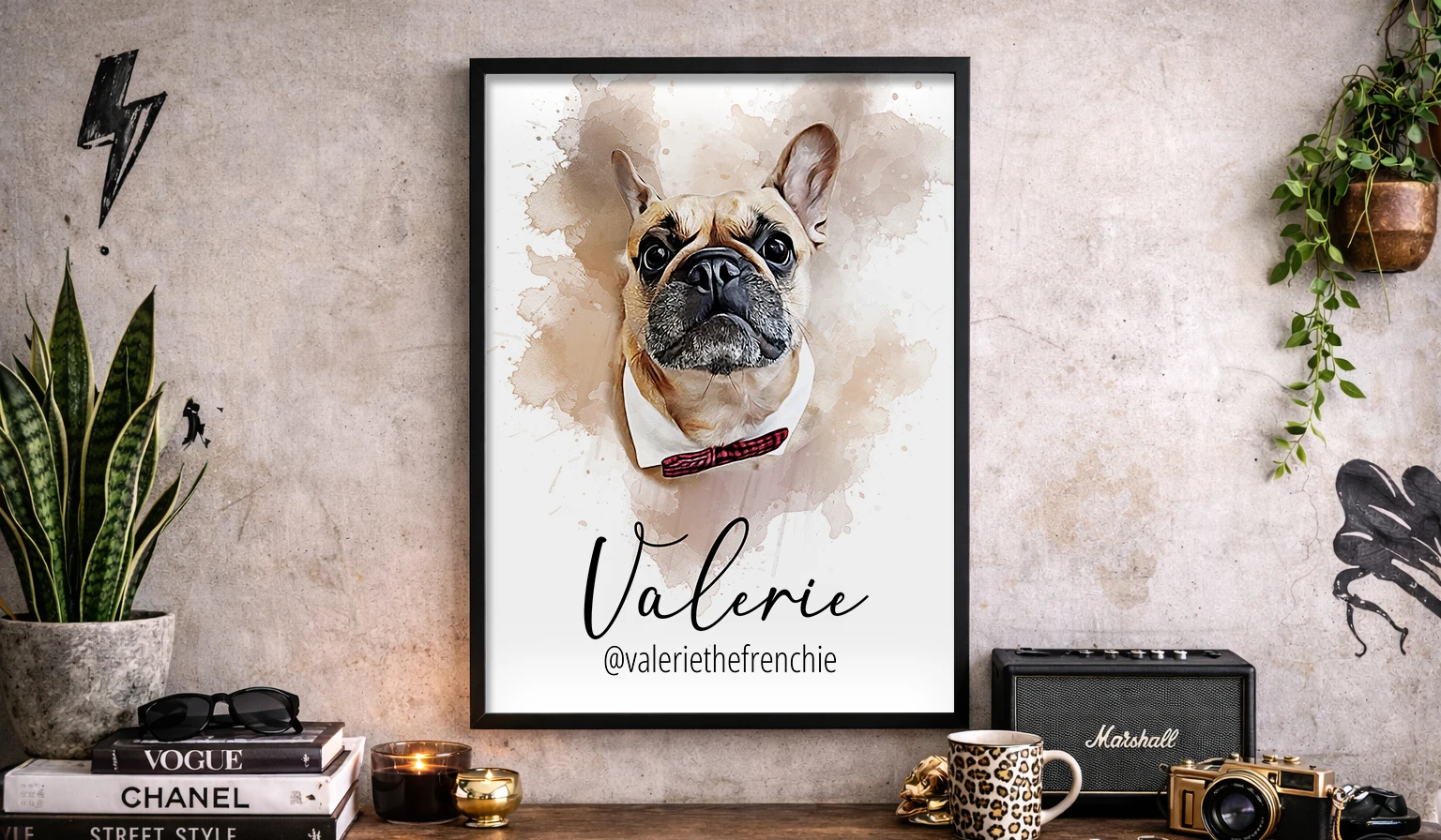Franska bulldoggen Valle avbildad i en akvarellmålning. Tavlan hänger i svart träram mot en betongvägg. Under tavlan är en möbel med en kamera, kaffekopp, en högtalare och en grön växt.